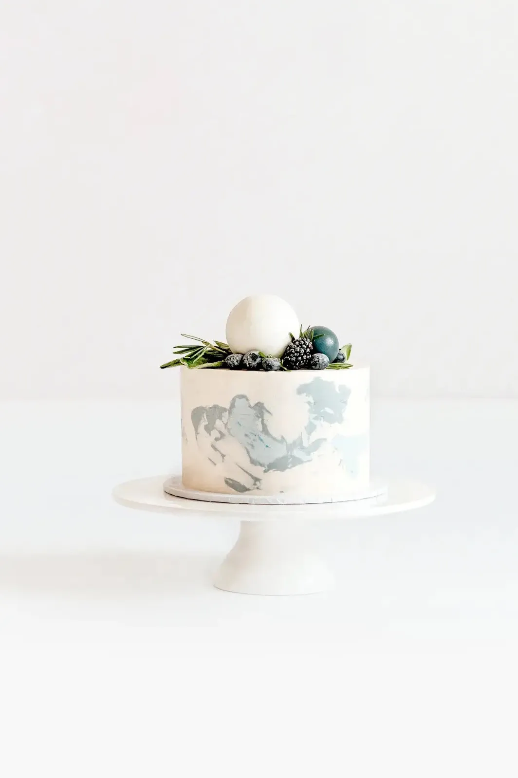 Elegante zweist&ouml;ckige Hochzeitstorte auf wei&szlig;em St&auml;nder mit grauem Vogeldesign und gr&uuml;ner Blattdeko auf der Oberseite.