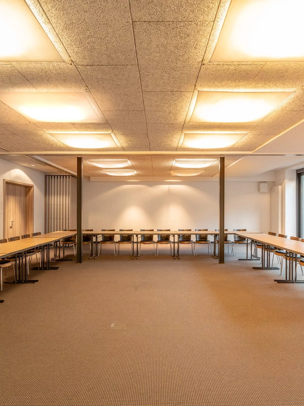 Gro&szlig;er, heller Veranstaltungsraum mit Kassettendecke und indirekter Beleuchtung, bestuhlt mit Konferenztischen.
