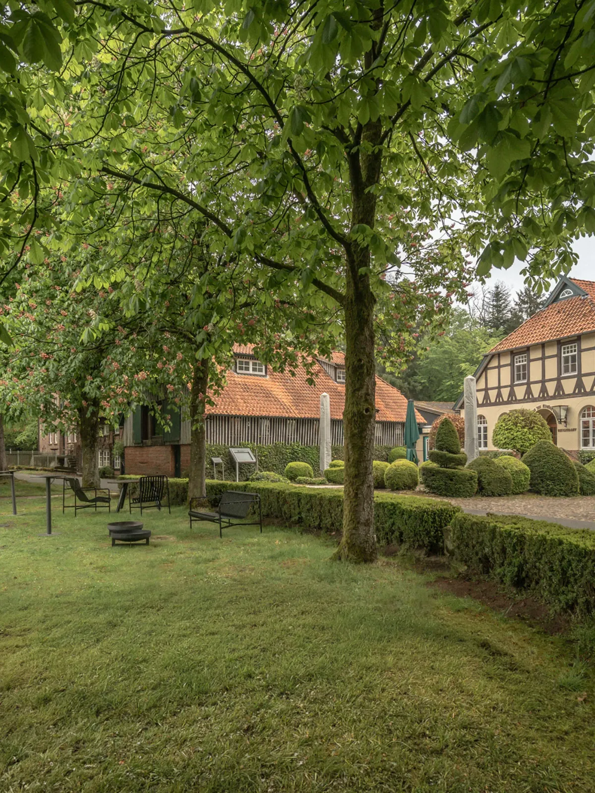 Gr&uuml;ne Parkanlage mit alten B&auml;umen, Rasenfl&auml;che und historischem Fachwerkhaus im Hintergrund.