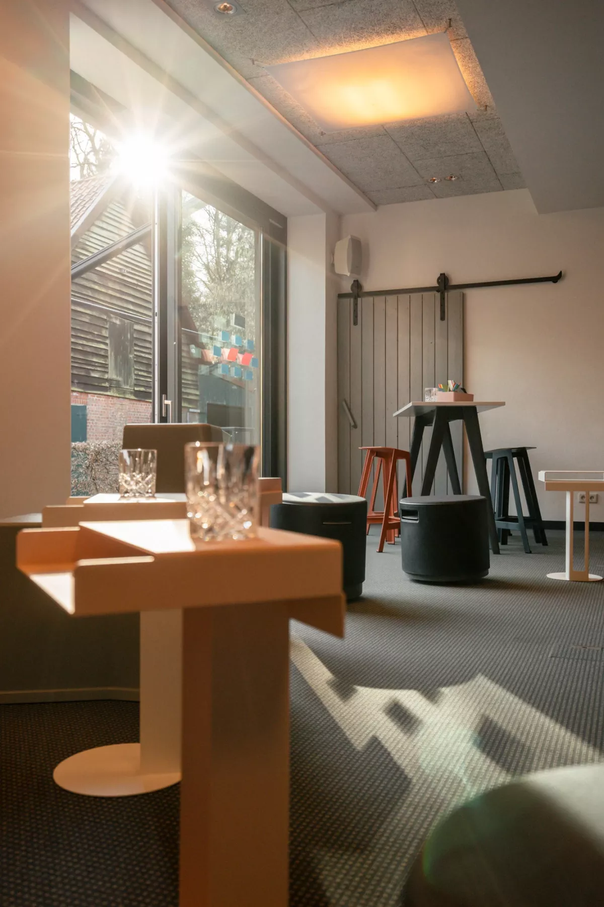 Heller Tagungs- und Workshopraum mit gro&szlig;em Fenster zur Gartenansicht und minimalistischer Einrichtung mit schwarzen Akzenten.