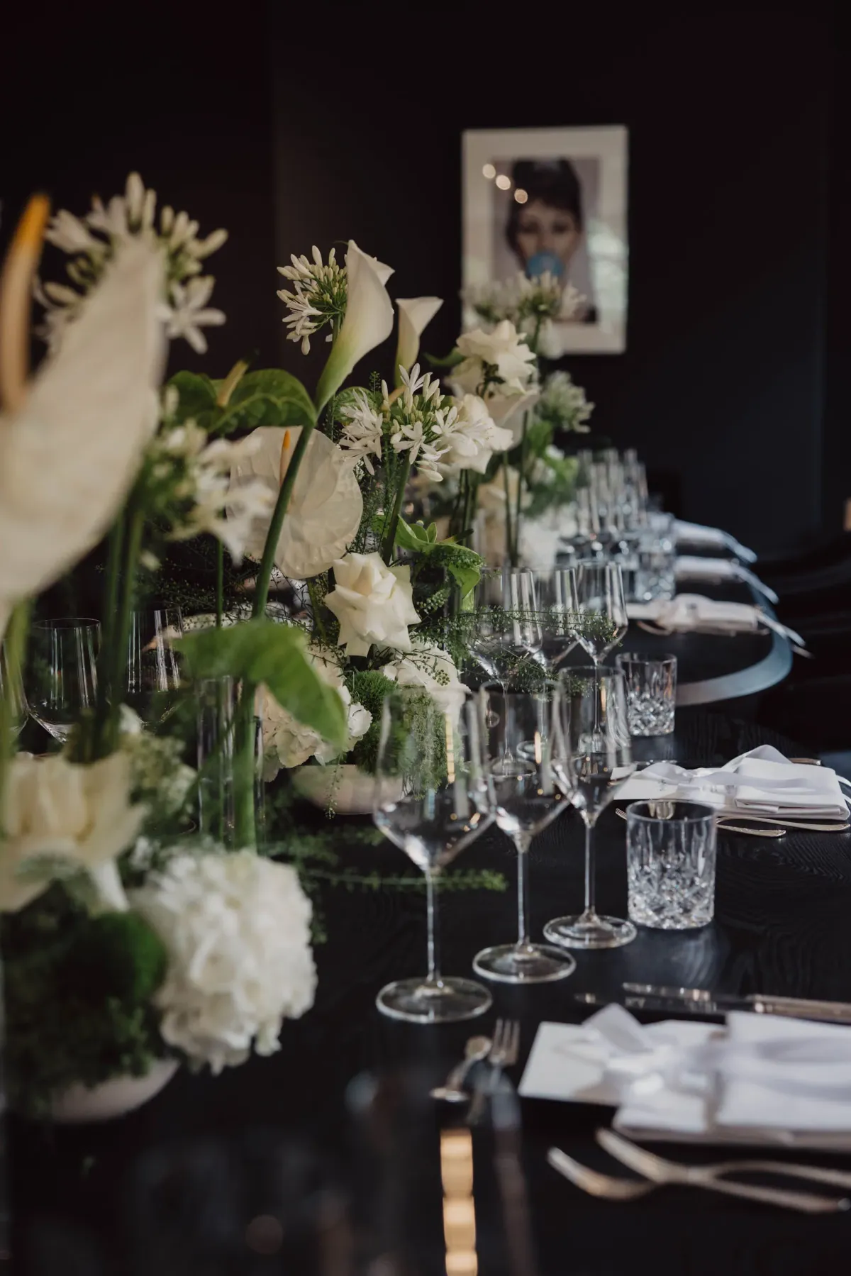 Elegant gedeckter Tisch mit wei&szlig;en Blumenarrangements, Kristallgl&auml;sern und feiner Besteckung vor dunklem Hintergrund.