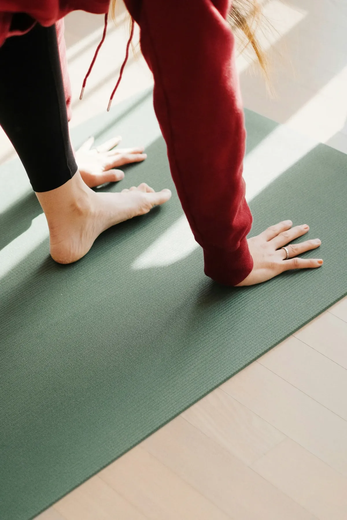Person in Sportkleidung steht barfu&szlig; auf einer gr&uuml;nen Yogamatte.