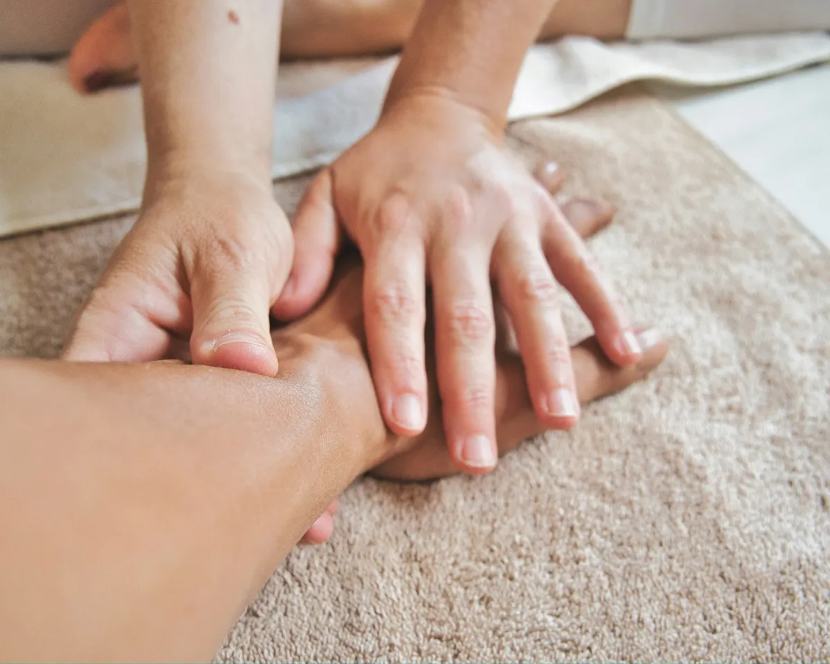Zwei H&auml;nde massieren Hand und Unterarm auf einem beigen Tuch.