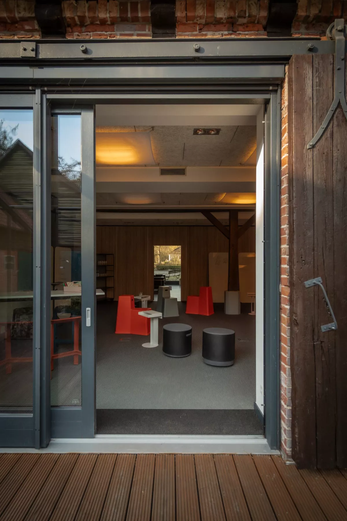 Moderne Glasschiebet&uuml;r f&uuml;hrt in einen eleganten Veranstaltungsraum mit roten St&uuml;hlen und dunklen Tischen auf grauem Boden.