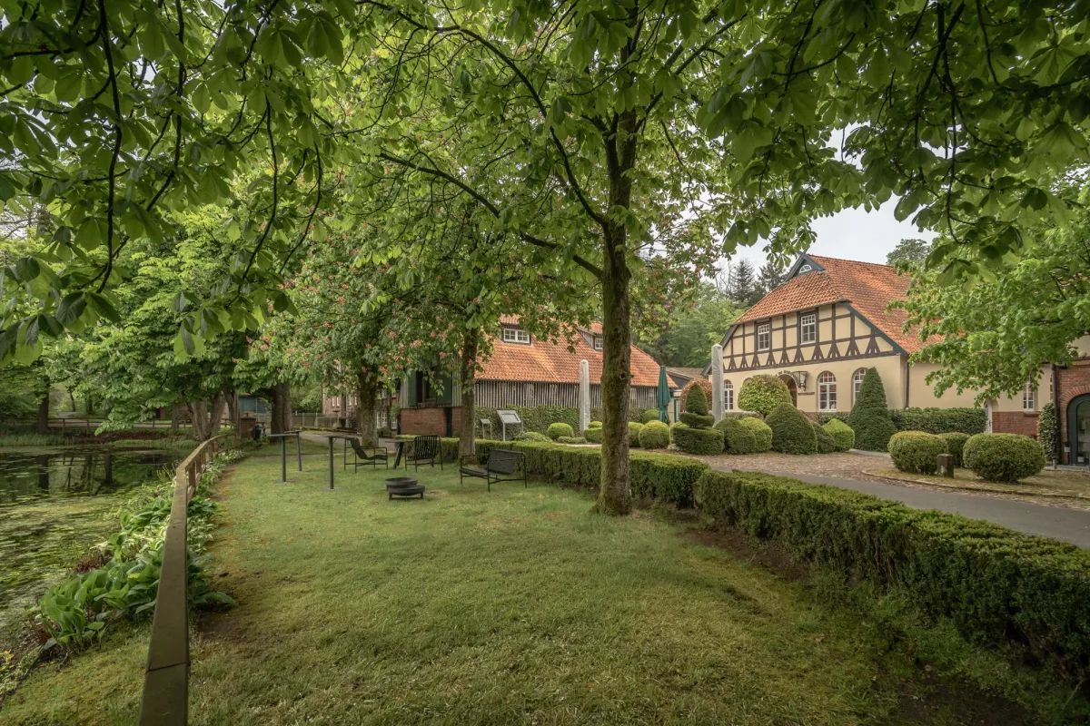 Gr&uuml;ne Parkanlage mit alten B&auml;umen, Rasenfl&auml;che und historischem Fachwerkhaus im Hintergrund.