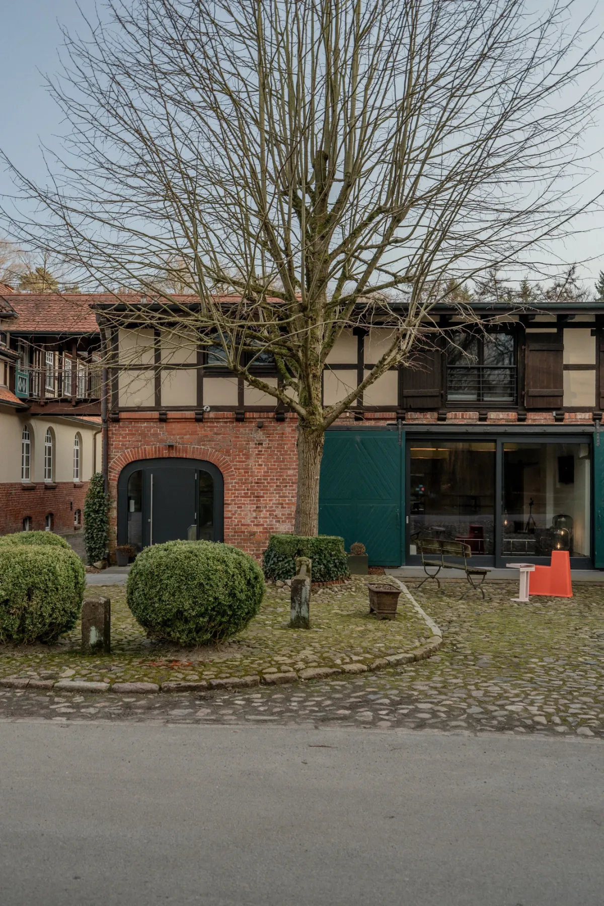 Historisches Fachwerkgeb&auml;ude mit Backsteinfl&uuml;gel, kahlem Baum und runden Buchsb&auml;umen.