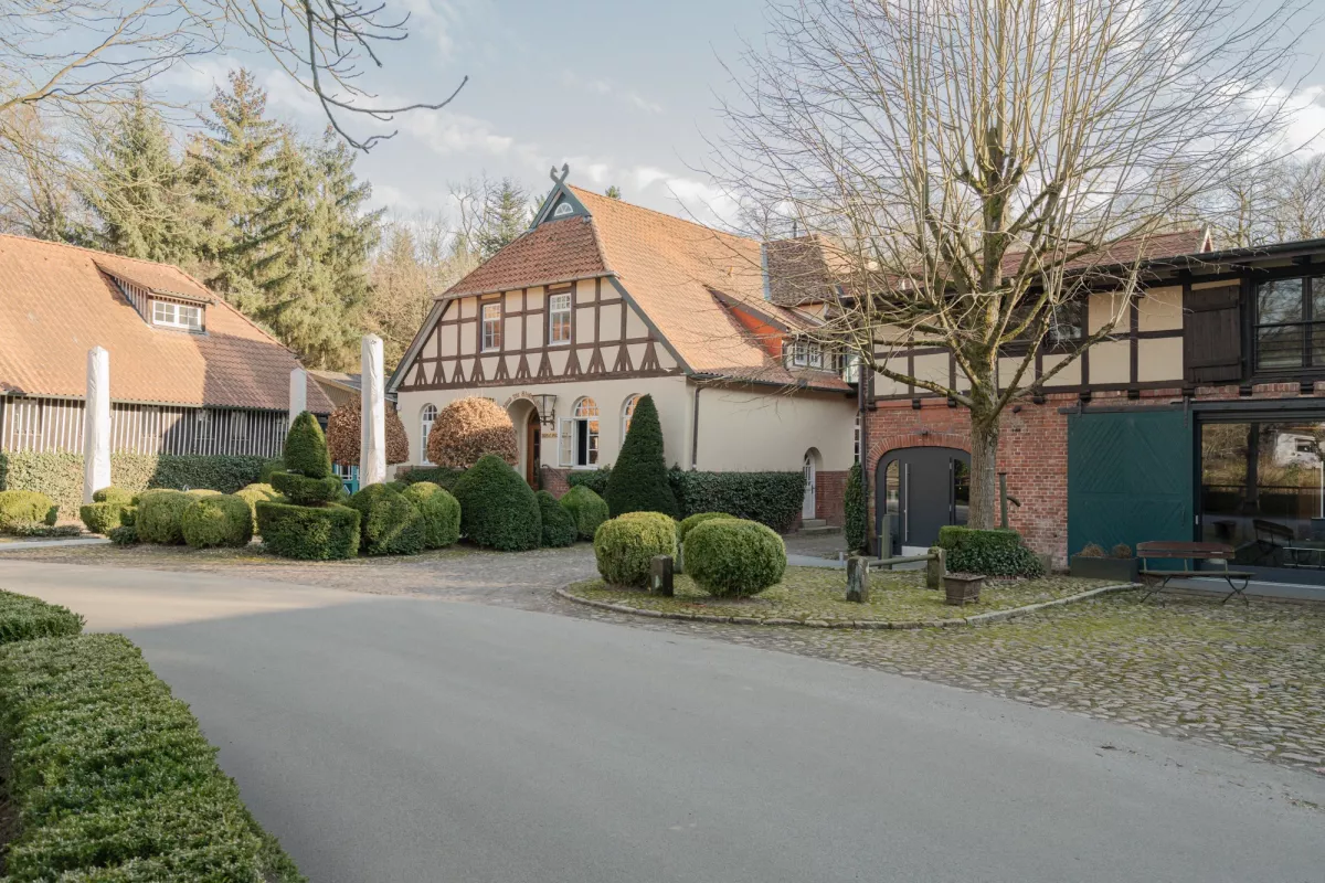 Historisches Fachwerkhaus mit Ziegeldach und gepflegter Terrasse, umgeben von B&auml;umen und gr&uuml;nen Hecken.