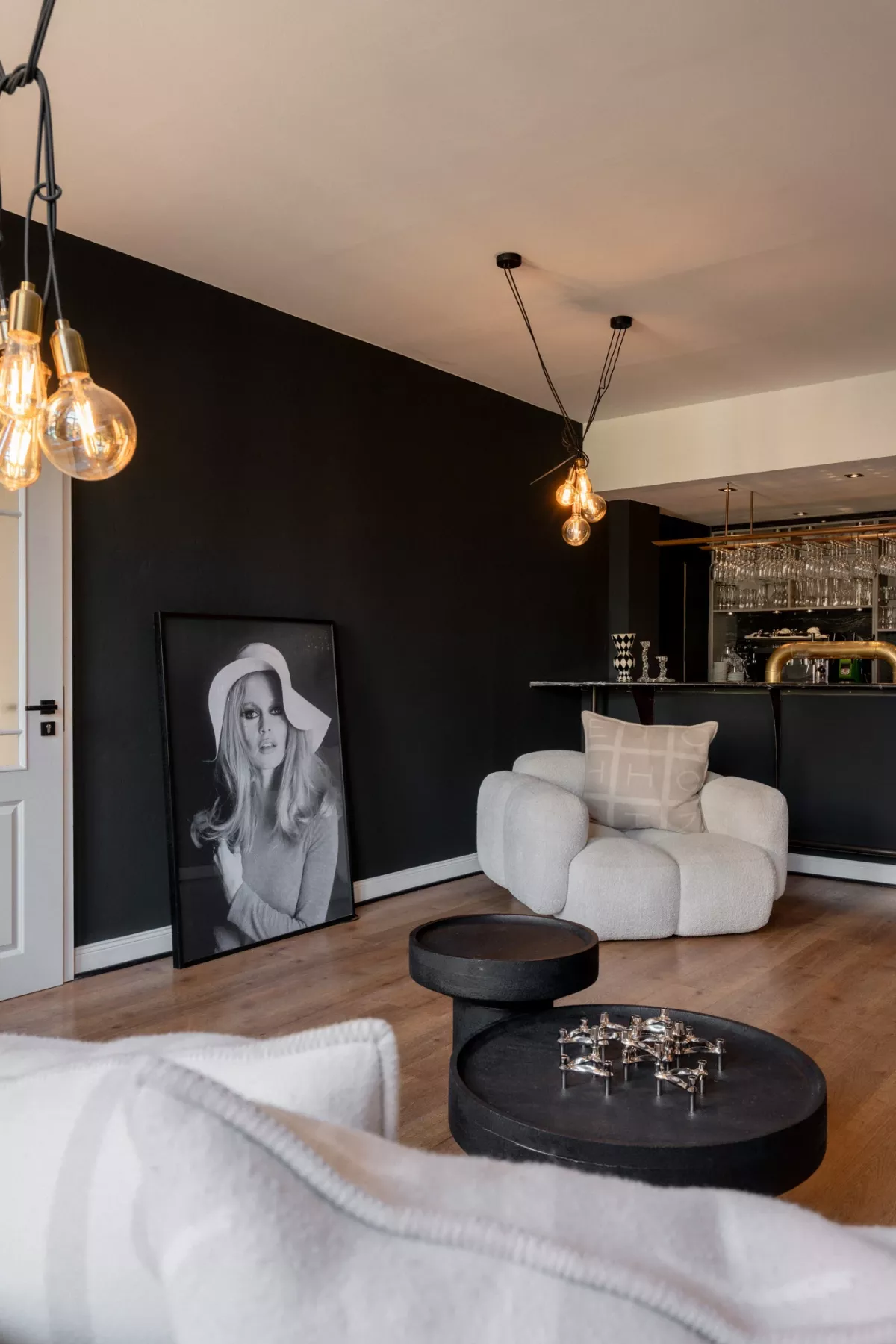 Moderner Barbereich mit schwarzer Akzentwand, cremefarbenem Sessel, schwarzen Couchtischen und Pendelleuchten.