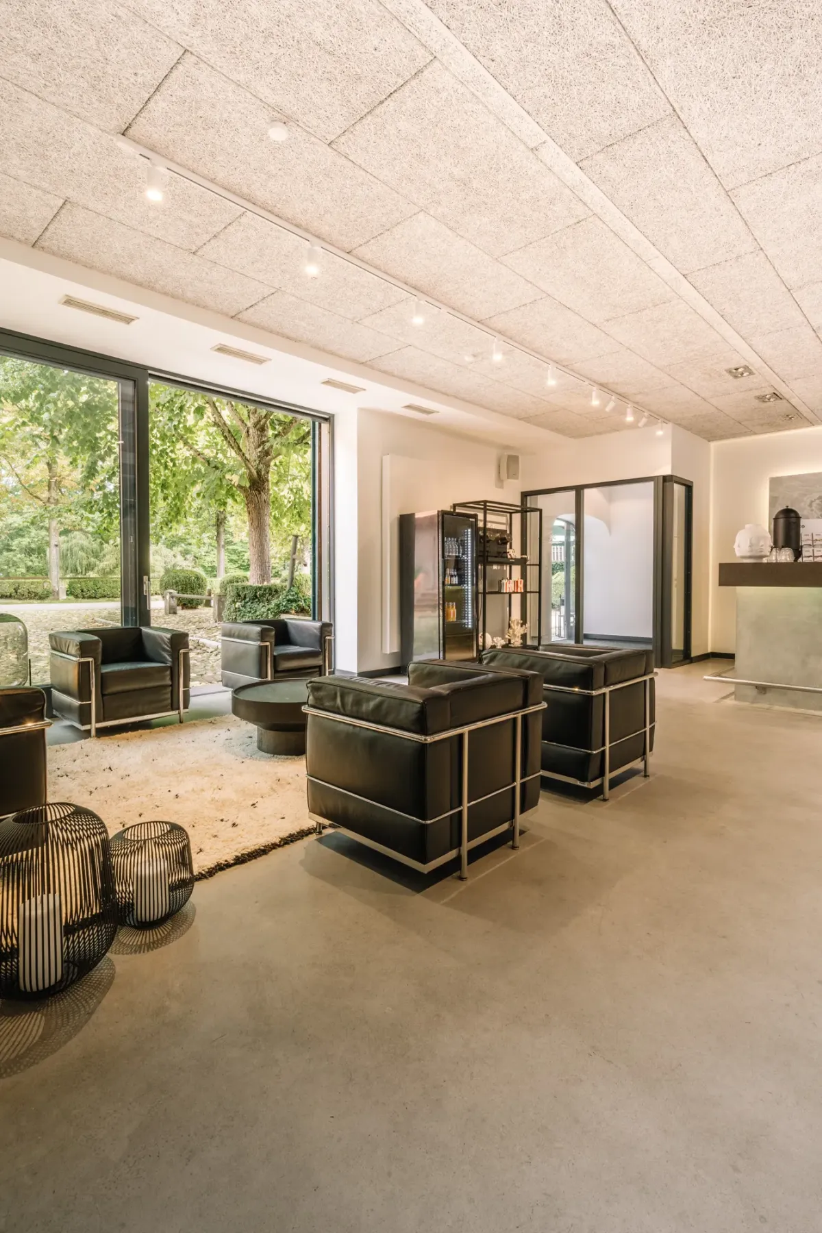 Moderner Loungebereich mit hellen Decken, schwarzen Designer-M&ouml;beln, gro&szlig;z&uuml;gigen Glast&uuml;ren zum Garten und minimalistischer Einrichtung f&uuml;r Events und Tagungen.