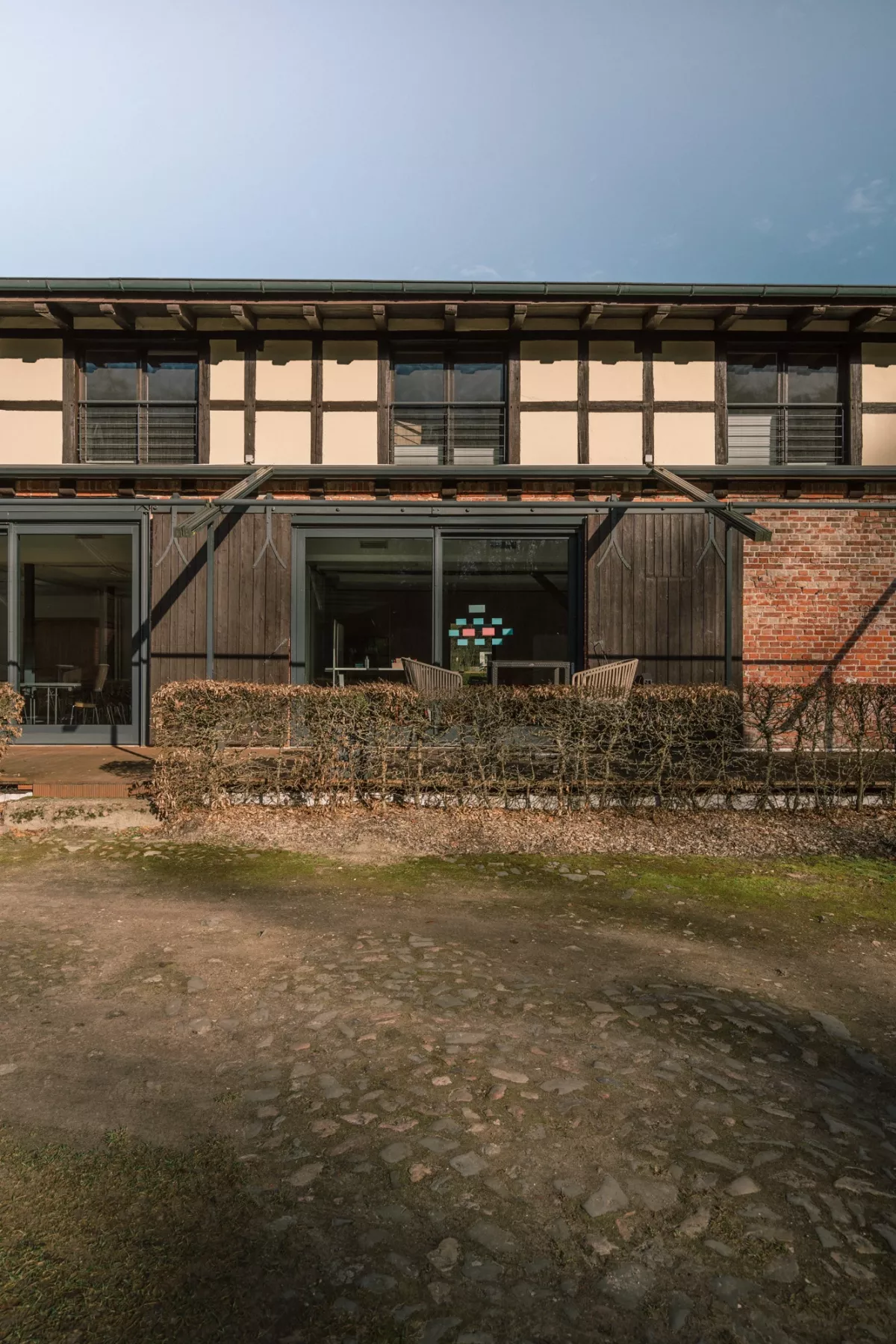 Moderne Eventlocation mit gro&szlig;z&uuml;gigen Glast&uuml;ren und Terrasse, rustikale Holz- und Backsteinarchitektur, umgeben von Natursteinen und gr&uuml;nem Rasen.