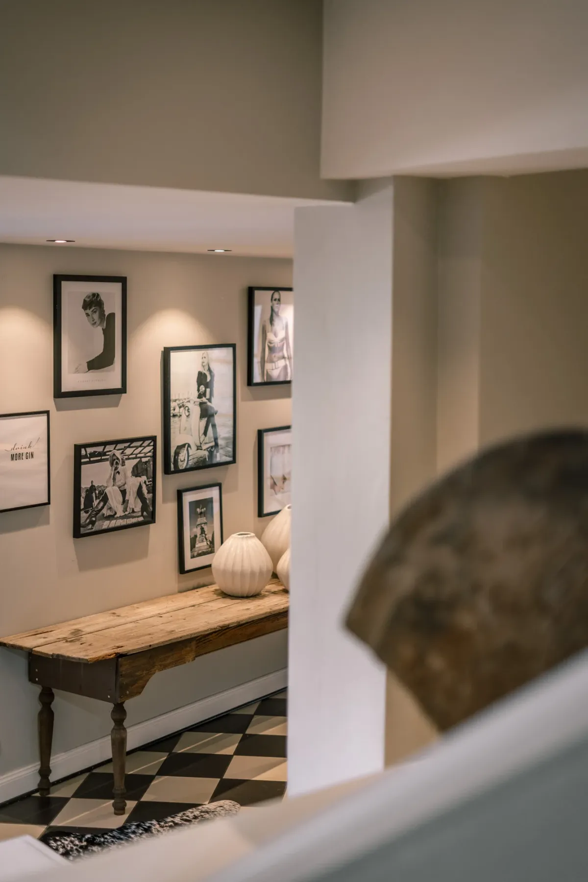 Eleganter Ausstellungsraum mit gerahmten Kunstdrucken an Wand, Holztisch mit gr&uuml;ner Vase und Schachbrettboden in klassischem Design.