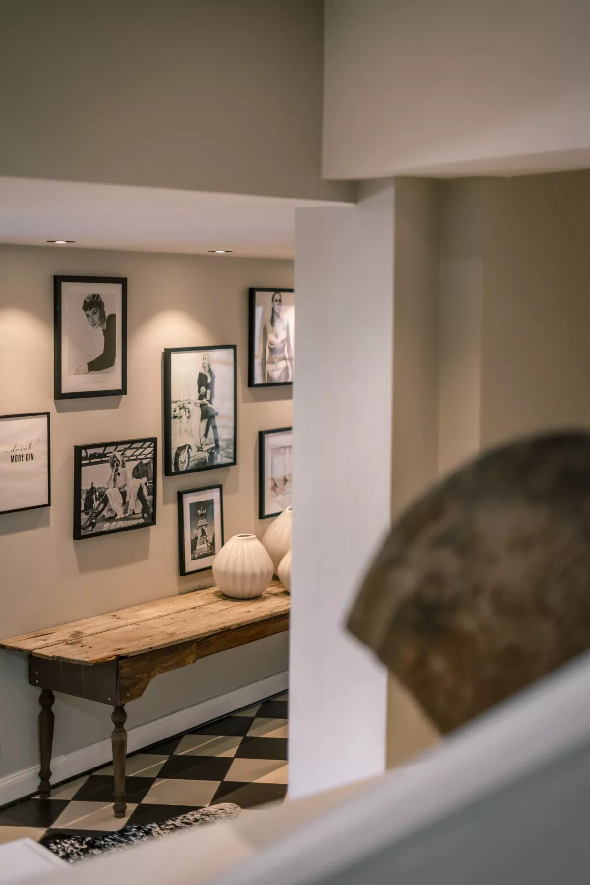 Eleganter Ausstellungsraum mit gerahmten Kunstdrucken an Wand, Holztisch mit gr&uuml;ner Vase und Schachbrettboden in klassischem Design.