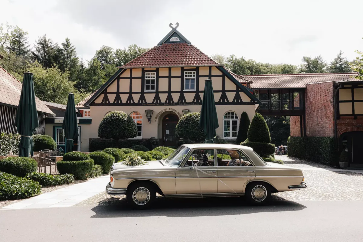Silberner Vintage-Mercedes parkt vor dem Hauptgeb&auml;ude von Klosterm&uuml;hle, einem Fachwerkhaus mit rotem Dach, dahinter sind Baumspitzen zu sehen.