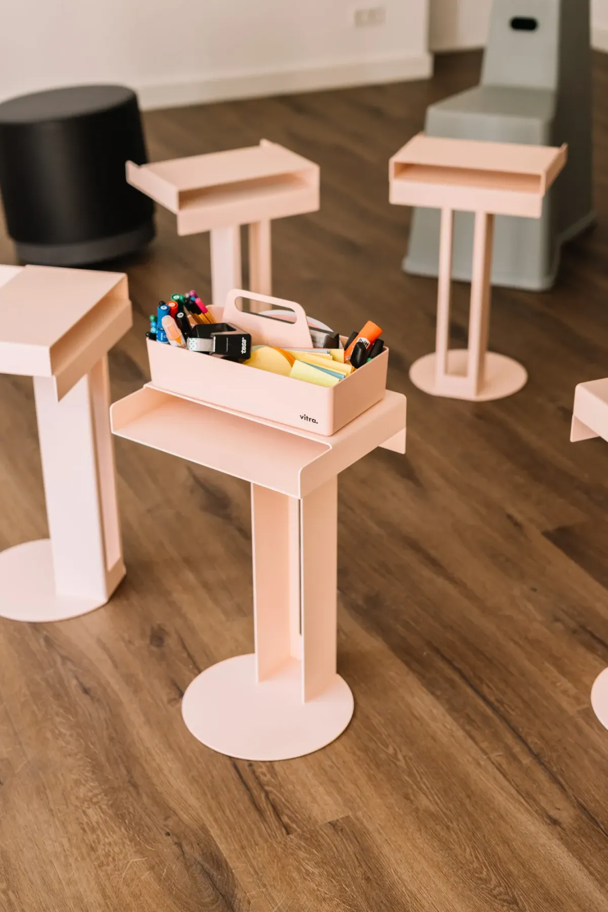 Hellrosa Stehtische mit Tabletop-Auslagen auf Holzboden, einer mit Stifthalter und Schreibmaterialien gef&uuml;llt, in modernem Eventlocation-Setting.