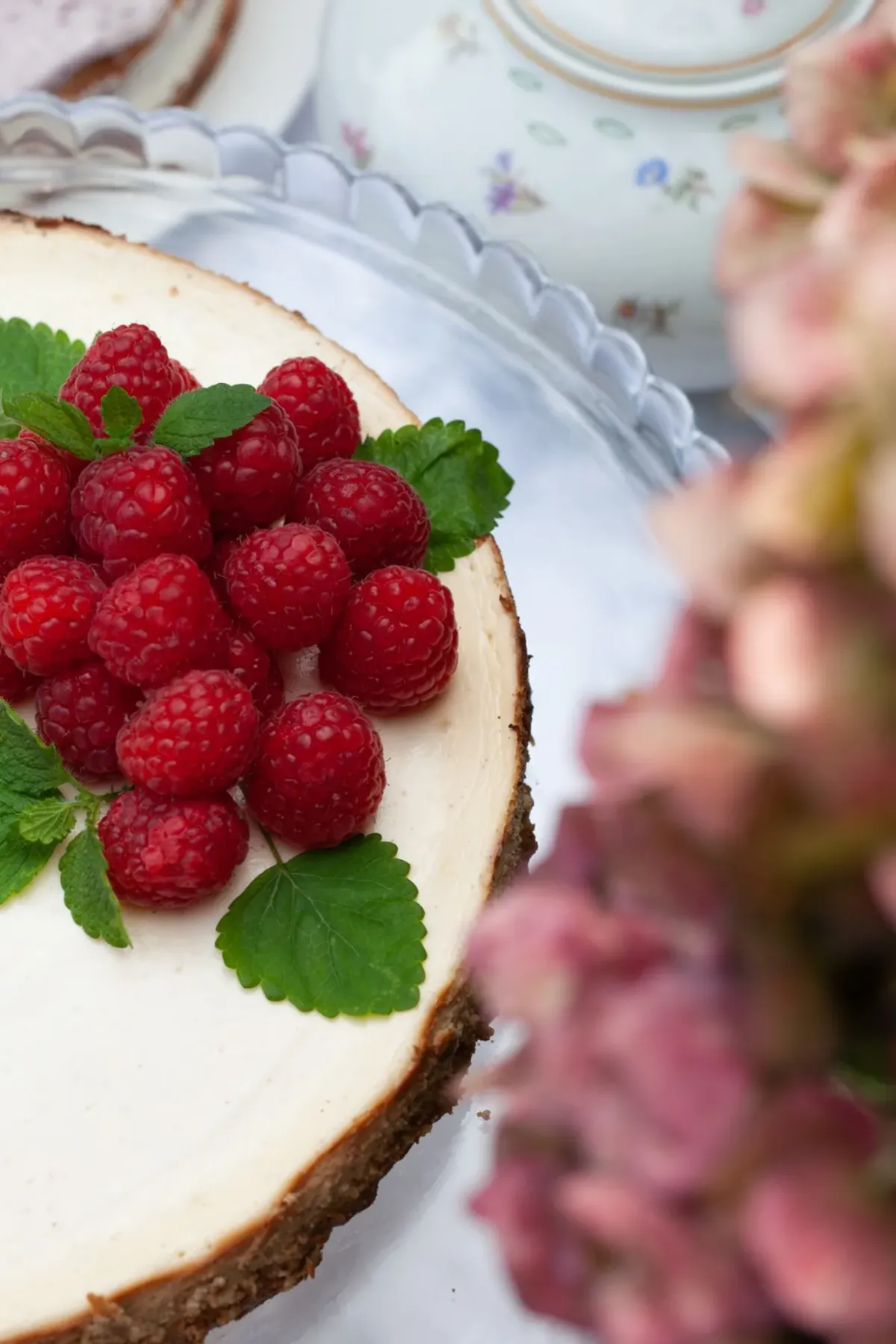 K&auml;sekuchen mit Pudding und frischen roten Himbeeren, garniert mit gr&uuml;nen Minzbl&auml;ttern auf wei&szlig;em Teller.