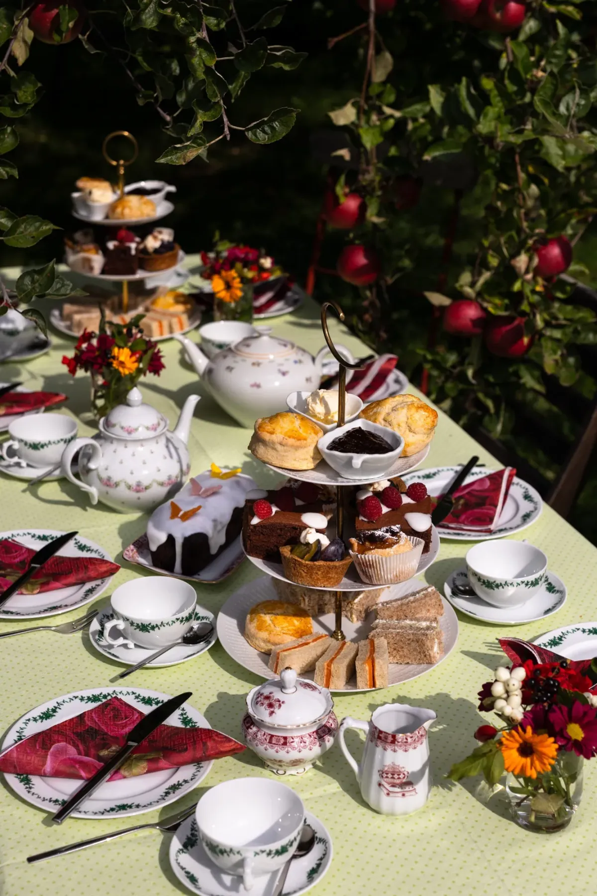 Festlich gedeckter Gartentisch unter bl&uuml;henden Rosenst&ouml;cken mit Kaffeeservice, Kuchen, Geb&auml;ck und Blumendekoration.