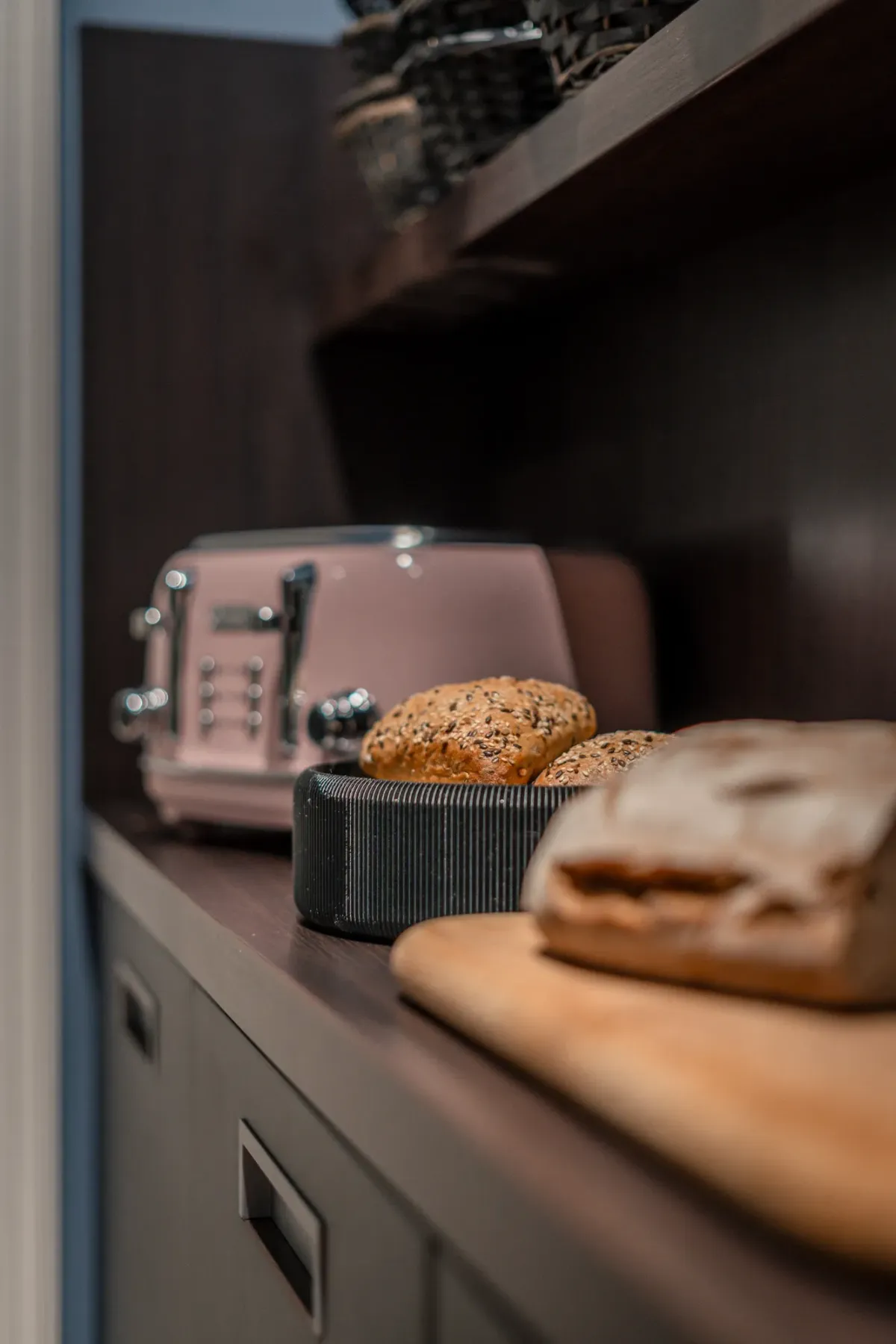 Br&ouml;tchen in schwarzem Korb auf K&uuml;chencountertop neben Toaster und Brot, moderne K&uuml;chenausstattung.