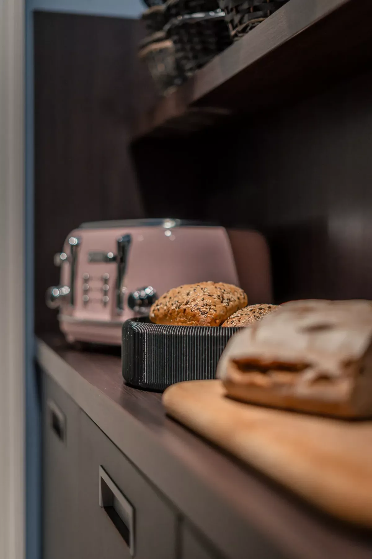 Br&ouml;tchen in schwarzem Korb auf K&uuml;chencountertop neben Toaster und Brot, moderne K&uuml;chenausstattung.