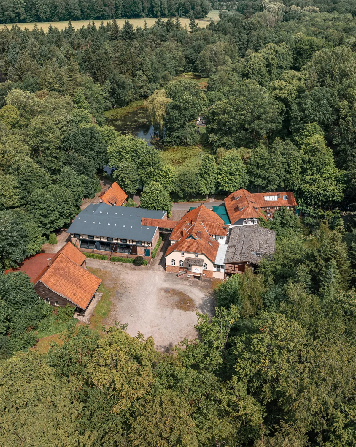 Luftaufnahme der Klosterm&uuml;hle mit mehreren Geb&auml;uden mit roten Ziegeld&auml;chern, umgeben von dichtem Wald und einem Weiher, ideal f&uuml;r Events und Feiern.